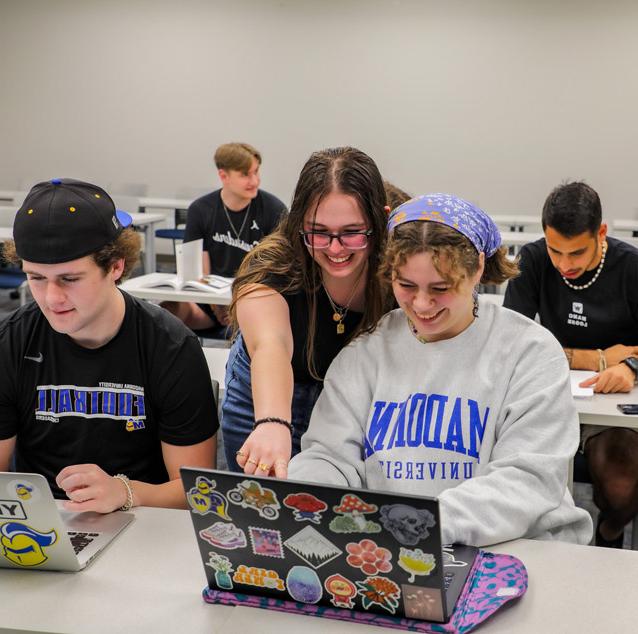 small group of students in classroom with two in the forefront reacting to something shown on a laptop screen